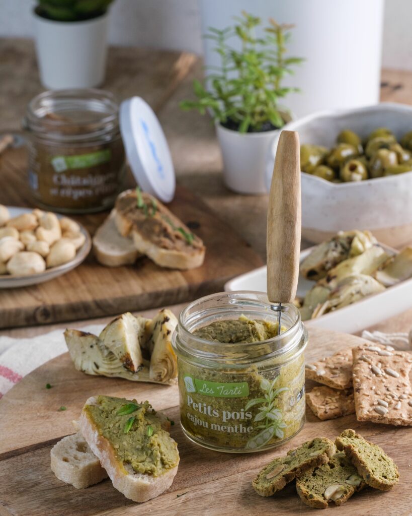 Tartinable apéro : bocal de tarti petits pois cajou menthe ouvert, présenté sur une planche en bois avec une tartine dressée à côté.