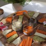 Petits toasts de tartinables veggies dont notre tarti betterave sésame sur une planche en bois avec bocaux ouverts