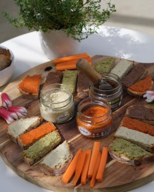 Petits toasts de tartinables veggies dont notre tarti betterave sésame sur une planche en bois avec bocaux ouverts