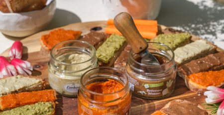 Assortiment de tartinables Maison Lembert présentés sur des toasts de pain, autour de bocaux ouverts, aux couleurs variées et appétissantes.