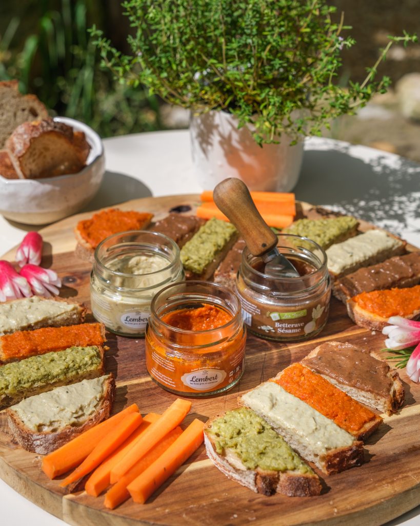 Tartinables apéro :Assortiment de tartinables proposés par la Maison Lembert, présentés sur des toasts de pain, autour de bocaux ouverts, aux couleurs variées et appétissantes.