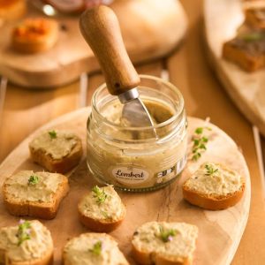 Petits toasts de tartinable artichaut à la truffe présentés sur une planche en bois, avec bocal ouvert –