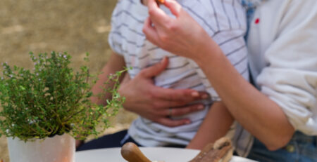 Idées apéritif été : enfant dégustant un tartinable sur les genoux de sa maman lors d’un apéritif d’été convivial avec des tartinables artisanaux colorés