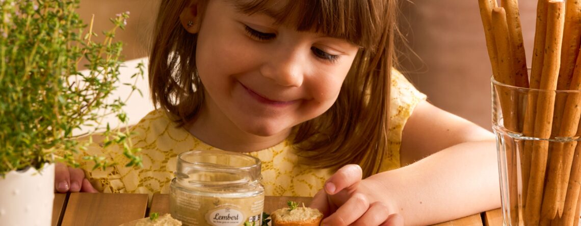 Petite fille souriante devant des tartinables apéro artisanaux sur planches en bois avec gressins