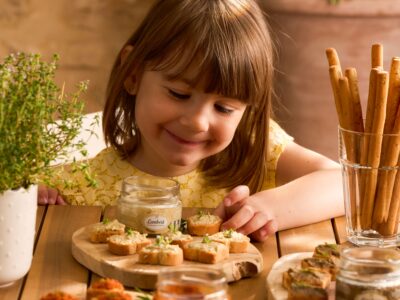Petite fille souriante devant des tartinables apéro artisanaux sur planches en bois avec gressins