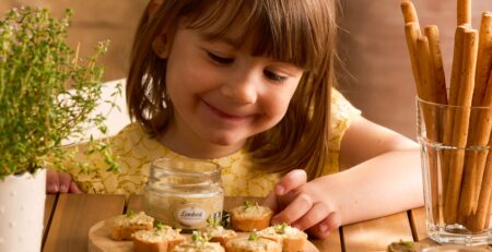 Petite fille souriante devant des tartinables apéro artisanaux sur planches en bois avec gressins