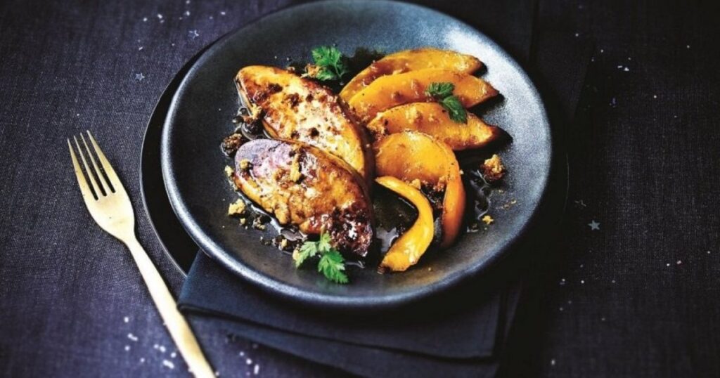 Recette foie gras à la poêle avec deux escalopes de foie gras poêlées servies dans une assiette noire accompagnées de légumes gourmands.