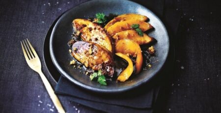 Recette foie gras à la poêle avec deux escalopes de foie gras poêlées servies dans une assiette noire accompagnées de légumes gourmands.