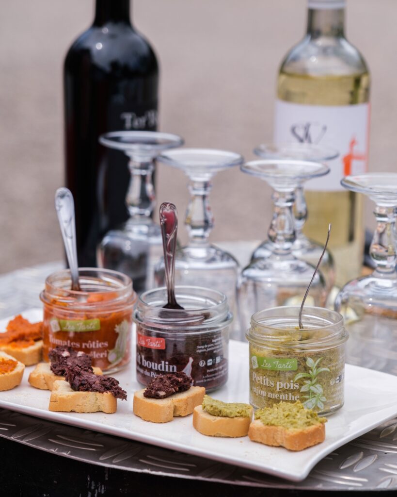 Trois tartinables artisanaux Maison Lembert présentés en bocaux ouverts avec leur cuillère, accompagnés de verres et de vins du Périgord.